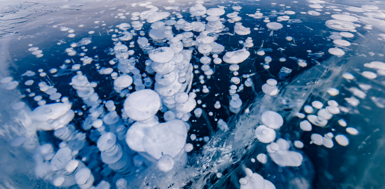 Gas methane bubbles frozen in winter ice of lake Baikal, abstract background.