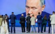 A crowd of people take pictures and watch a largescreen broadcast of President Vladimir Putin.