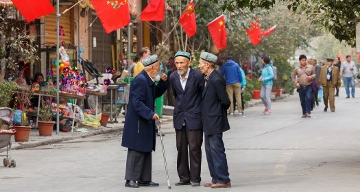Three older men stand in a street lined with Chinese flags.