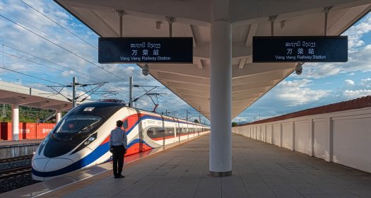 A conductor stands next to a high speed train on an empty platform.