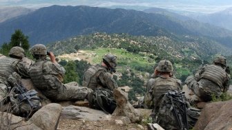 Five U.S. soldiers sit on a ridge looking out at a valley in Afghanistan.