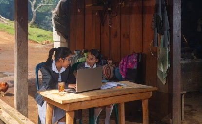 Two girls sitting in front of a computer in the rural outdoors.