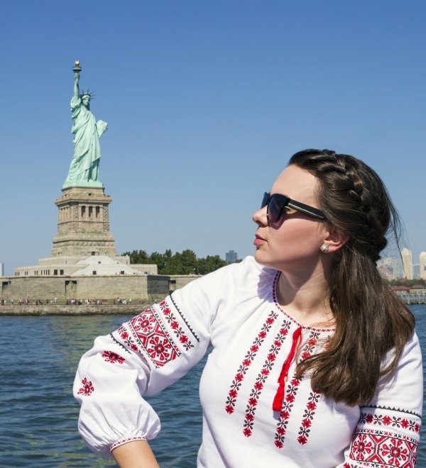 Woman in traditional Ukrainian dress sitting in front of the statue of Liberty