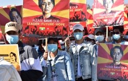 A crowd of protestors wearing surgical masks carry signs reading Please Save our Leader - Future - Hope with a photo of Aung San Suu Kyi