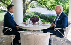 President Moon Jae-in sits opposite of President Joe Biden at an outdoor table.