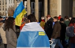 Berlin, Germany - November 13, 2022: Male demonstrator covered with a white-blue-white flag at a rally in solidarity with Ukraine against Russian Imperialism at Brandenburg Gate in Berlin